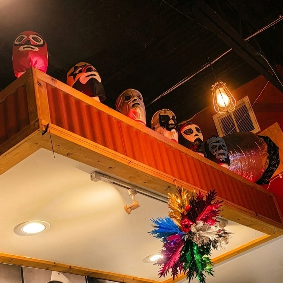 Lucha Libre masks displayed on a high shelf with a red wall and colorful decoration below.