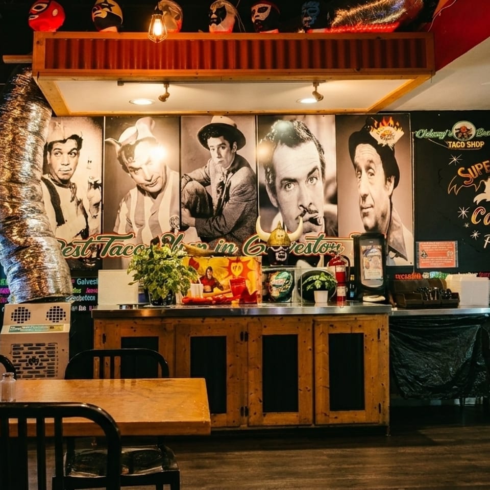 Interior of a taco shop with tables, a counter, and large black and white portraits on the wall.